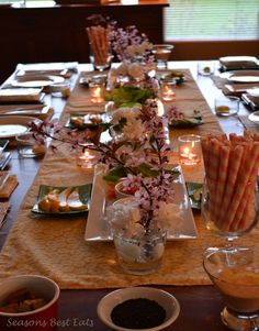 the table is set with candles, plates and flowers in vases on each side