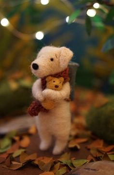 a stuffed bear holding a teddy bear on top of leaves and lights in the background