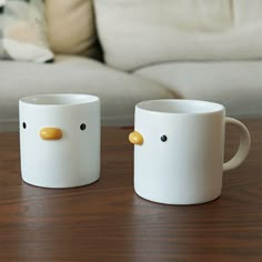 two coffee mugs sitting on top of a wooden table next to a white couch