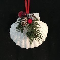 a christmas ornament hanging from a red ribbon on a black background with pine cones and berries