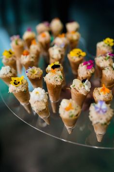 there are many ice cream cones with flowers in them on the glass plate and one is filled with cake