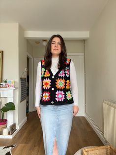 a woman standing in a hallway wearing a black sweater vest with colorful flowers on it