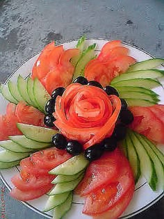 a white plate topped with watermelon and black olives next to an orange flower