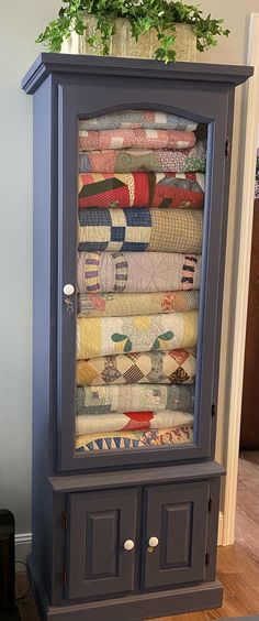 an old china cabinet with quilts on it and a potted plant in the corner