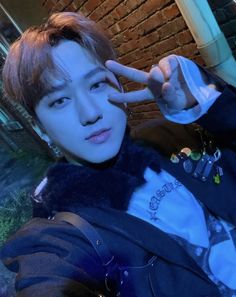 a young man making the peace sign with his hand while standing in front of a brick wall