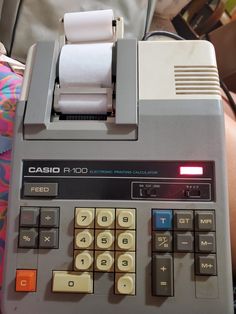 an old cash register machine sitting on top of a bed next to a person's arm