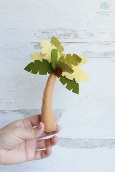 a hand holding a paper palm tree with yellow and green leaves on it's tip