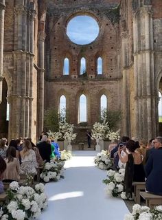 a wedding ceremony in an old church with white flowers and greenery on the aisle