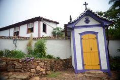 a small white house with a yellow door and purple trim on the side of it