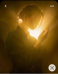 a woman is holding her hands together in the dark with light coming from behind her