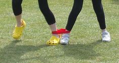 two people wearing yellow shoes and black pants standing in the grass with their feet up