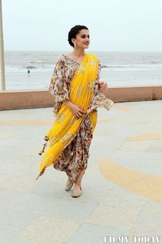 a woman in a yellow sari walking along the beach with her hand on her hip