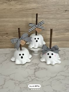 three white ghost candles with black and white bows on them sitting on a marble counter