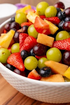 a white bowl filled with fruit on top of a wooden table