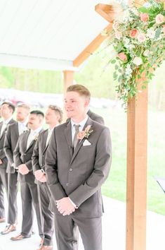 a group of men standing next to each other in front of a wooden structure with flowers on it