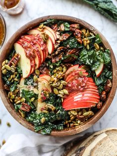 a wooden bowl filled with apples, spinach and other food on top of a table