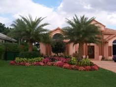 a house with palm trees and flowers in the front yard, surrounded by lush green grass