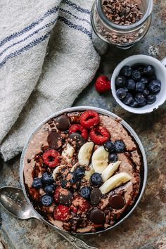 a bowl filled with fruit and chocolate on top of a table next to two bowls of granola