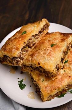 two pieces of meat filled pastry on a white plate next to a fork and napkin