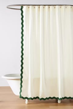 a white shower curtain with green scalloped trim on the edge and bottom, in front of a bathtub