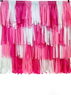 pink and white streamers hanging on a clothes line in front of a white wall