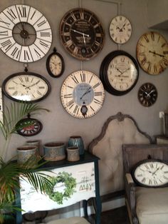 many clocks are on the wall above a chair and table in front of a couch