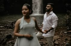 a man and woman standing in front of a waterfall