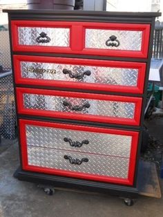 a red and black dresser sitting on top of a metal floor next to a fence