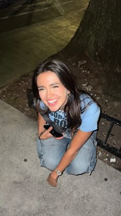 a woman squatting on the ground next to a tree