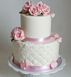 a three tiered white cake with pink flowers on the top and bottom, sitting on a platter