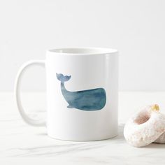 a white coffee mug with a blue whale design on it next to a donut