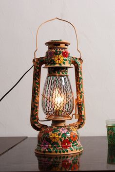 a colorful lantern sitting on top of a table next to a glass cup and candle