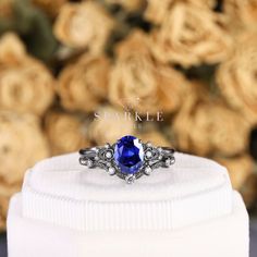 a blue stone ring sitting on top of a white box next to some gold roses