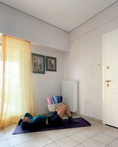 a woman laying on top of a purple mat in front of a window next to a radiator