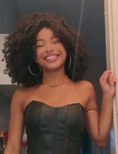 a woman with curly hair standing in front of a mirror and smiling at the camera