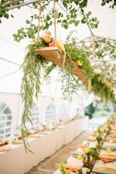 a long table is set up with flowers and greenery hanging from it's ceiling