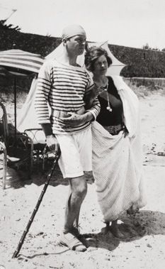 an old black and white photo of two people standing on the beach, one wearing a hat