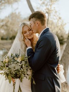 a bride and groom standing next to each other in front of a tree with flowers