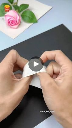 a person is cutting paper with scissors on a black and white striped tablecloth next to a pink rose