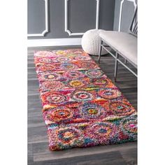 a multicolored rug on the floor in a living room with a bench and gray walls