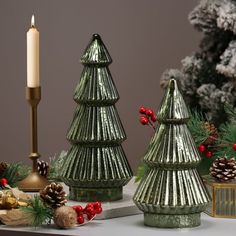 three christmas trees on a table next to a lit candle and other holiday decor items