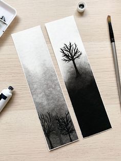 two bookmarks with trees drawn on them next to a brush and watercolor palette