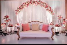 a white couch sitting under a flower covered arch with pink and red flowers on it