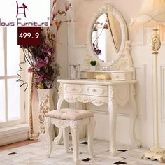 a white vanity with a mirror and stool in a room next to a vase filled with flowers