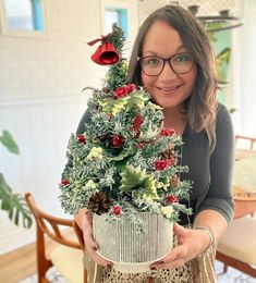 a woman is holding a christmas tree in her hands and smiling at the camera while wearing glasses