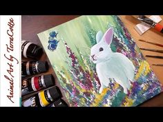 a painting of a white rabbit on a table with paintbrushes and watercolors