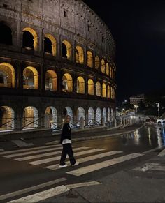 a person walking across a street in front of an old building at night with lights on