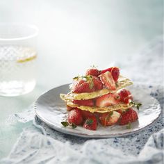 a stack of pancakes topped with strawberries on a plate next to a glass of water