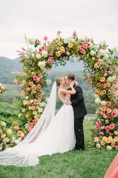 Bride and groom sharing a romantic kiss under a floral arch with pink, peach, and white blooms, set against the Blue Ridge Mountains at their outdoor wedding ceremony. Pink Ceremony Arch, Floral Arch Wedding Outdoor, Pink And Peach Wedding, Pippin Hill Wedding, Wedding Ceremony Seating, Modern Wedding Ceremony, Hill Wedding, Romantic Kiss