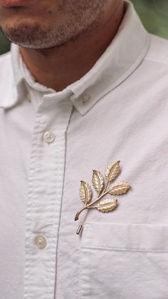 a man wearing a white shirt with a gold leaf brooch on his lapel